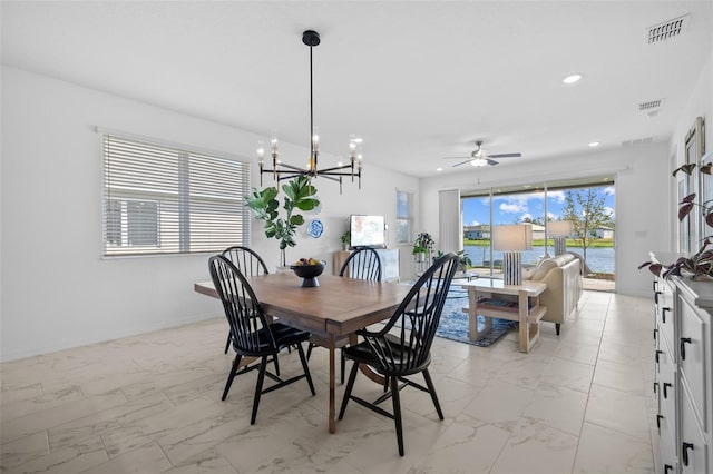 dining space featuring a water view and ceiling fan with notable chandelier