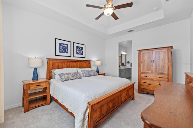 carpeted bedroom with a raised ceiling, ensuite bath, and ceiling fan