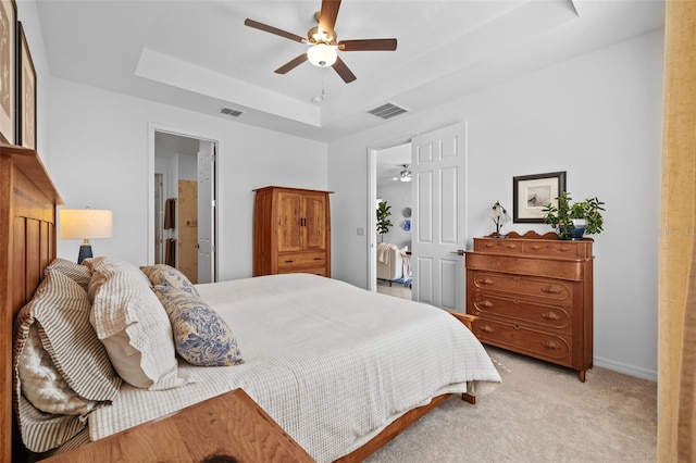 bedroom with ceiling fan, light carpet, connected bathroom, and a tray ceiling