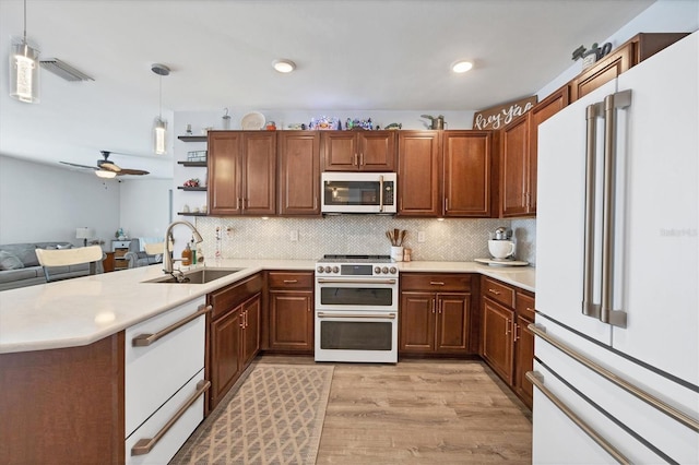 kitchen with high end appliances, sink, kitchen peninsula, pendant lighting, and light wood-type flooring