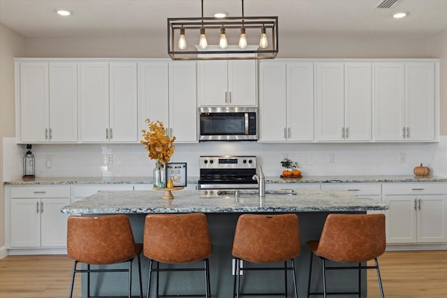 kitchen featuring light stone countertops, appliances with stainless steel finishes, light hardwood / wood-style floors, and white cabinetry