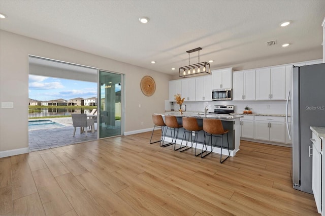 kitchen featuring a kitchen island with sink, pendant lighting, stainless steel appliances, and light hardwood / wood-style flooring