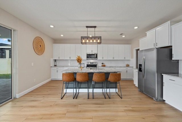 kitchen with light stone countertops, appliances with stainless steel finishes, decorative light fixtures, and white cabinetry