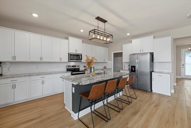 kitchen with white cabinets, stainless steel appliances, light hardwood / wood-style flooring, and a kitchen island with sink