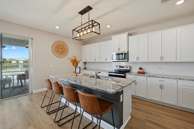 kitchen with white cabinets, stainless steel appliances, hanging light fixtures, and an island with sink