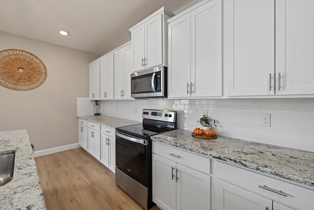 kitchen featuring tasteful backsplash, light stone counters, stainless steel appliances, light hardwood / wood-style flooring, and white cabinetry