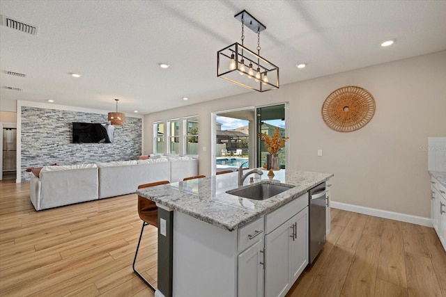 kitchen with white cabinetry, a center island with sink, dishwasher, and light wood-type flooring