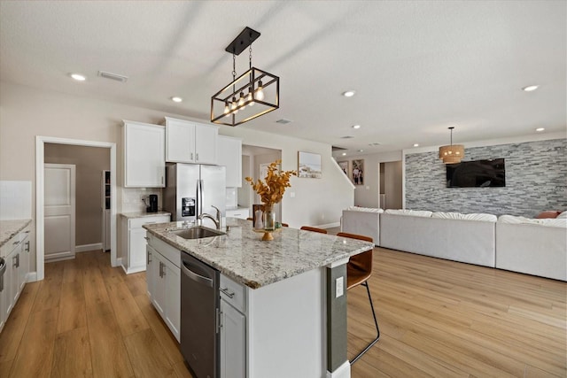 kitchen with a center island with sink, sink, light wood-type flooring, appliances with stainless steel finishes, and white cabinetry