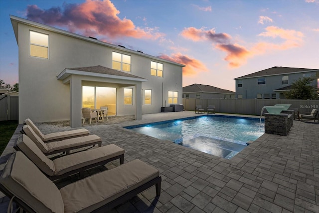 pool at dusk with pool water feature, a patio area, and an in ground hot tub