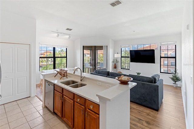 kitchen with brown cabinetry, visible vents, a sink, stainless steel dishwasher, and open floor plan