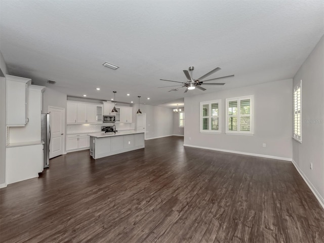 unfurnished living room featuring ceiling fan with notable chandelier, a textured ceiling, and dark wood-type flooring