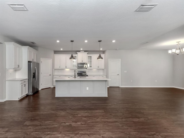 kitchen featuring a kitchen island with sink, dark wood-type flooring, white cabinets, hanging light fixtures, and stainless steel appliances