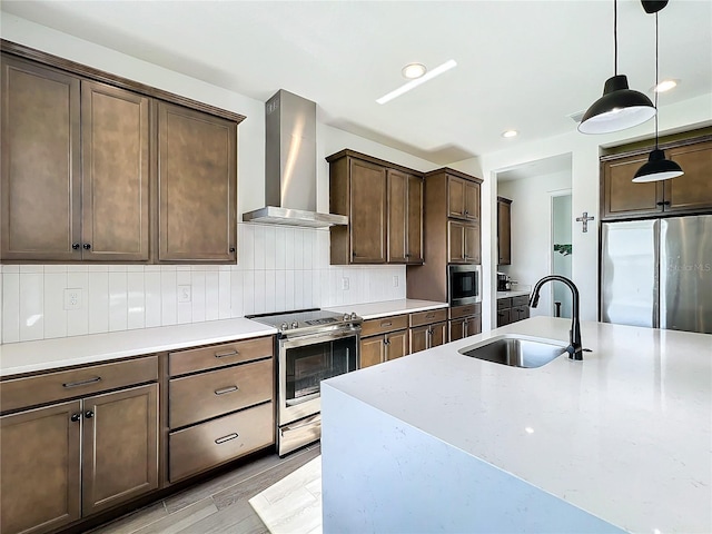 kitchen featuring appliances with stainless steel finishes, wall chimney exhaust hood, sink, decorative light fixtures, and light stone countertops