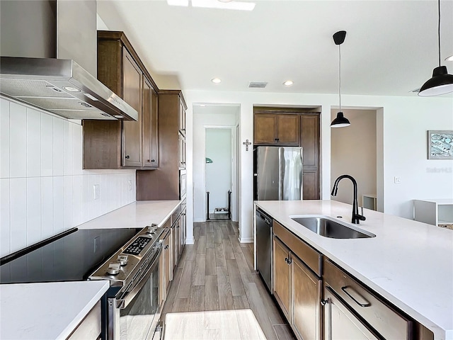 kitchen featuring wall chimney exhaust hood, sink, decorative light fixtures, light hardwood / wood-style floors, and stainless steel appliances