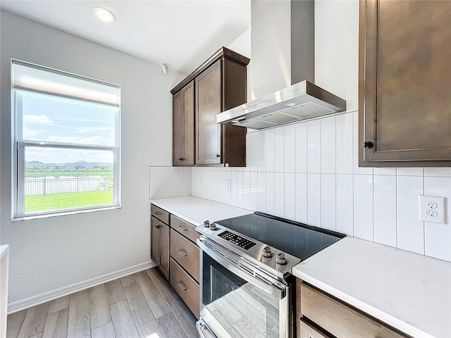 kitchen with dark brown cabinets, light hardwood / wood-style flooring, stainless steel electric range oven, extractor fan, and decorative backsplash