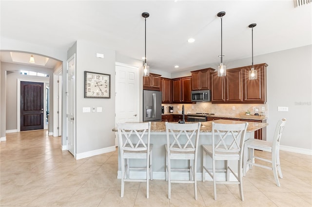 kitchen featuring a kitchen island with sink, a breakfast bar area, decorative light fixtures, light stone counters, and stainless steel appliances