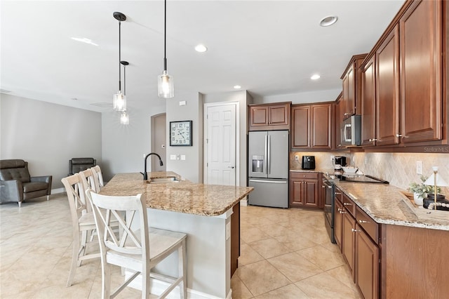 kitchen featuring sink, hanging light fixtures, stainless steel appliances, light stone counters, and an island with sink