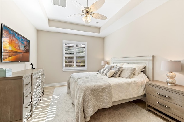 bedroom with light hardwood / wood-style floors, a raised ceiling, and ceiling fan