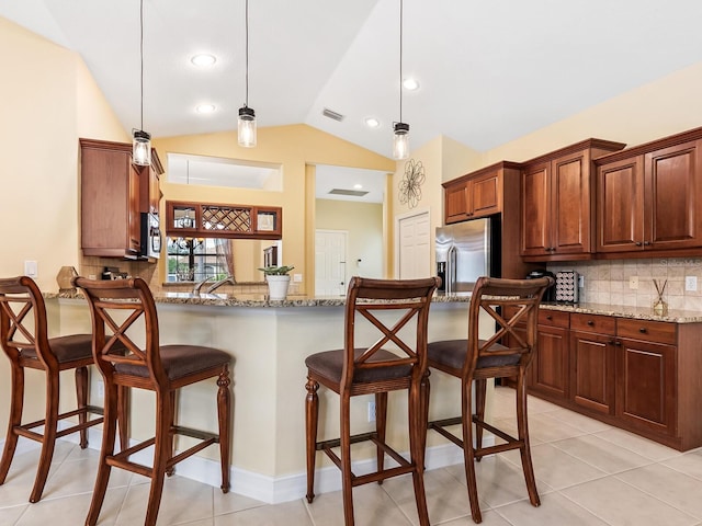 kitchen featuring appliances with stainless steel finishes, light stone counters, hanging light fixtures, and lofted ceiling