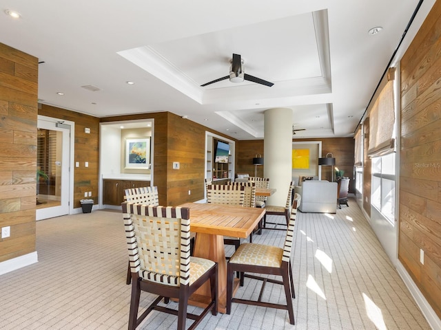 dining space with wooden walls, ceiling fan, and a raised ceiling