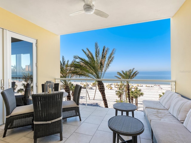 view of patio / terrace featuring a balcony, ceiling fan, a water view, and a view of the beach