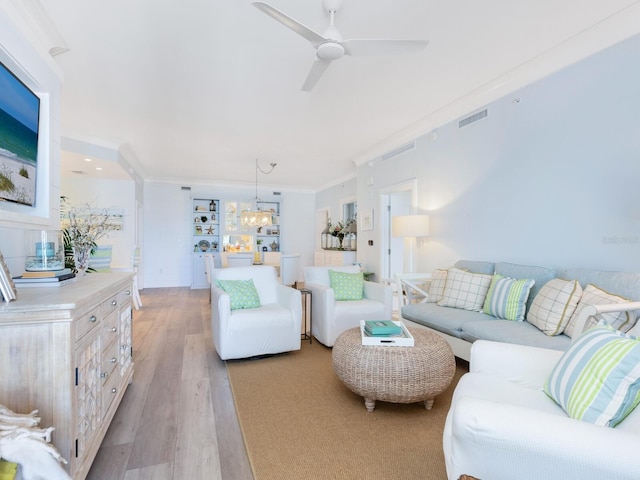 living room featuring ceiling fan with notable chandelier, ornamental molding, and light wood-type flooring