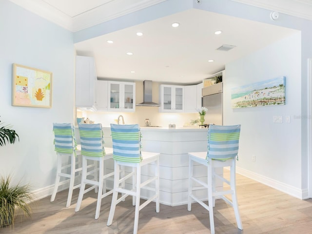 kitchen with crown molding, white cabinetry, stainless steel built in refrigerator, light hardwood / wood-style floors, and wall chimney exhaust hood