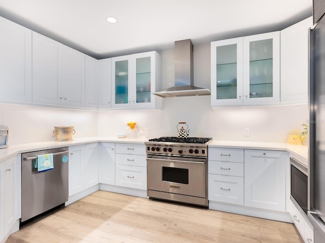 kitchen with stainless steel appliances, white cabinets, wall chimney range hood, and light wood-type flooring