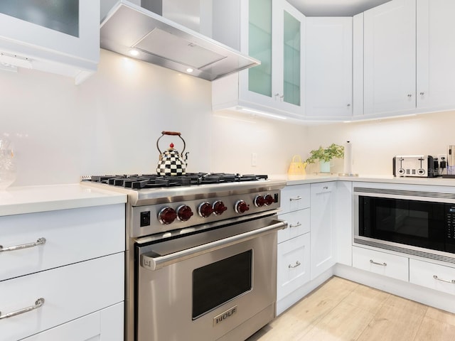 kitchen with stainless steel appliances, white cabinetry, light hardwood / wood-style floors, and ventilation hood