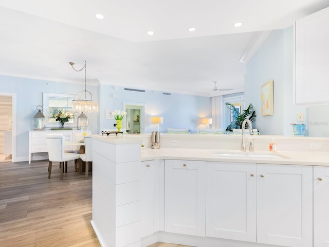 kitchen with decorative light fixtures, white cabinetry, sink, ornamental molding, and light hardwood / wood-style floors