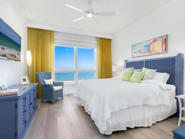 bedroom featuring ceiling fan, light hardwood / wood-style floors, a water view, and crown molding