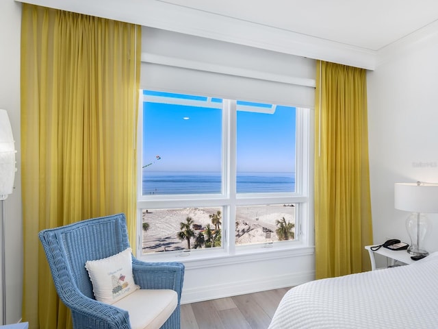 bedroom featuring ornamental molding, light hardwood / wood-style flooring, a water view, and a view of the beach