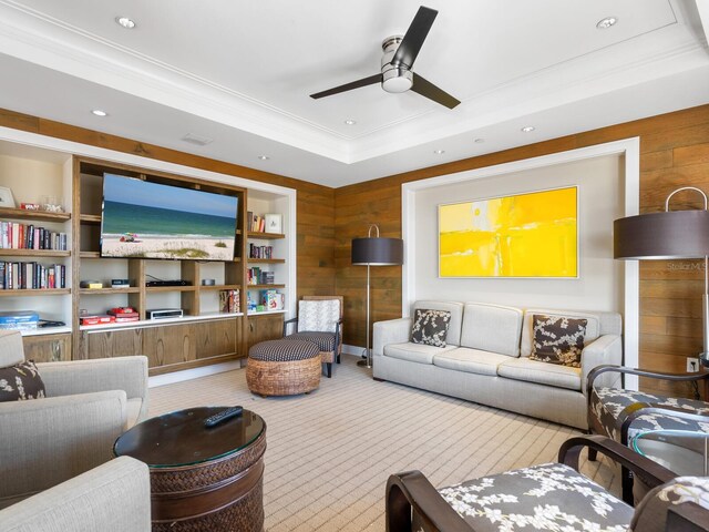 living room with ornamental molding, a raised ceiling, ceiling fan, and wooden walls