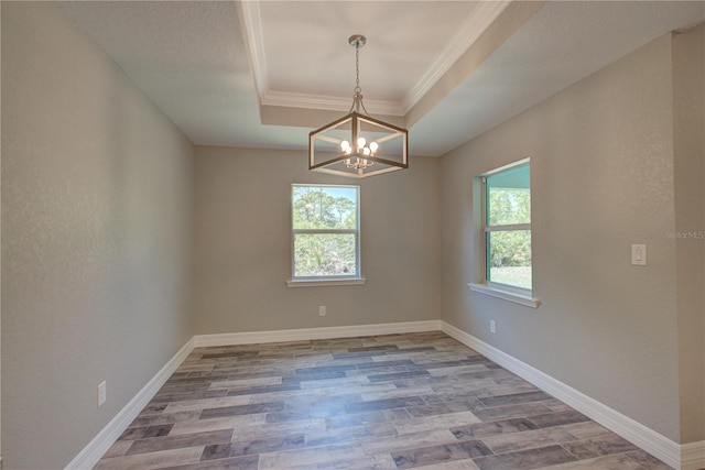 empty room with light hardwood / wood-style floors, a raised ceiling, crown molding, and an inviting chandelier