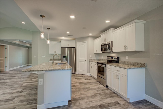 kitchen with stainless steel appliances, sink, pendant lighting, white cabinets, and an island with sink