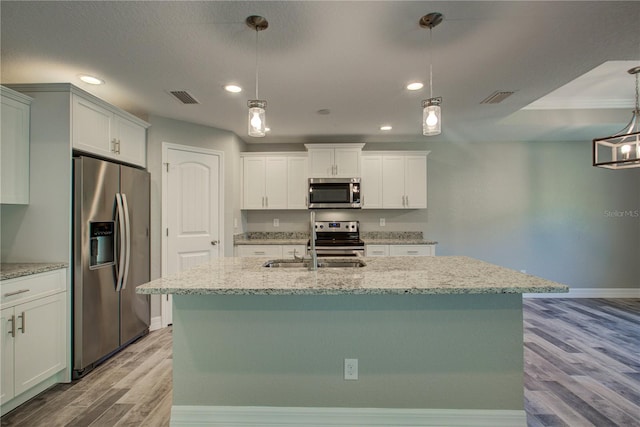 kitchen with stainless steel appliances, pendant lighting, a center island with sink, light hardwood / wood-style floors, and white cabinetry