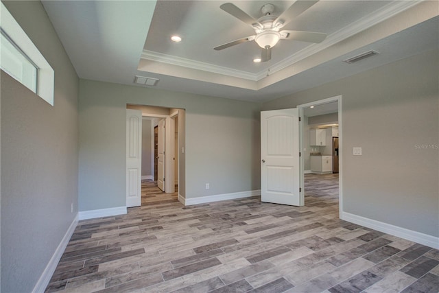 spare room with a tray ceiling, light hardwood / wood-style flooring, ceiling fan, and ornamental molding