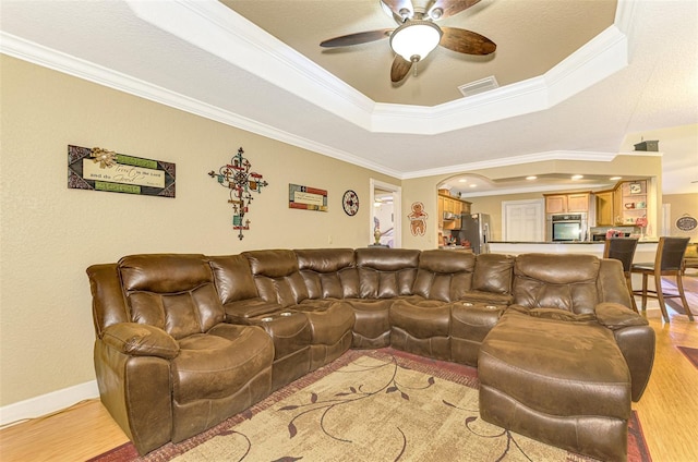 living room featuring light wood-type flooring, a tray ceiling, ceiling fan, and crown molding