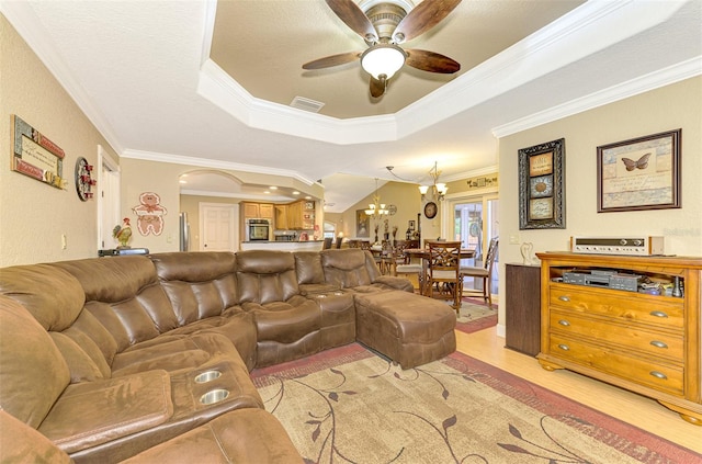 living room featuring ceiling fan with notable chandelier, light hardwood / wood-style floors, a raised ceiling, and crown molding