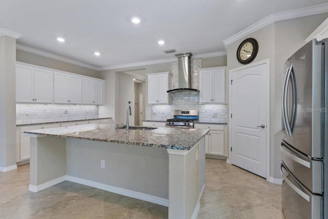 kitchen with a kitchen island with sink, white cabinets, wall chimney range hood, sink, and appliances with stainless steel finishes