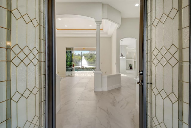 interior space with ornate columns, crown molding, a tray ceiling, and an inviting chandelier