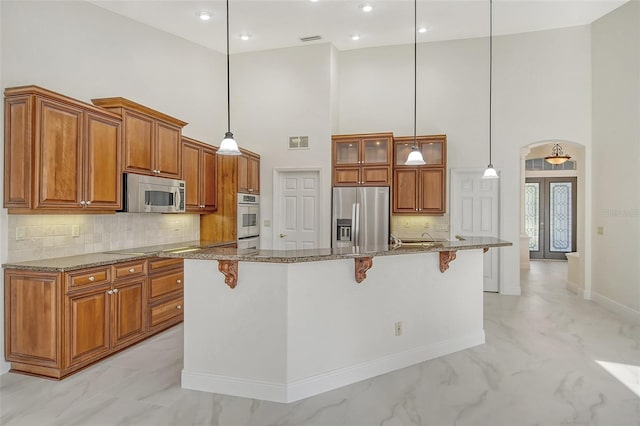 kitchen with a center island with sink, a breakfast bar area, appliances with stainless steel finishes, dark stone countertops, and french doors