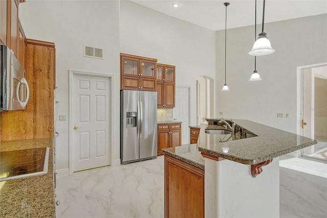 kitchen with decorative light fixtures, stainless steel appliances, dark stone countertops, sink, and a breakfast bar area