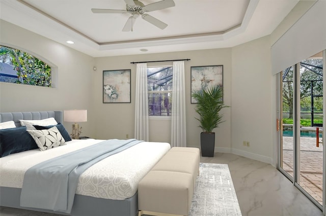 bedroom featuring ceiling fan, access to exterior, a tray ceiling, and multiple windows