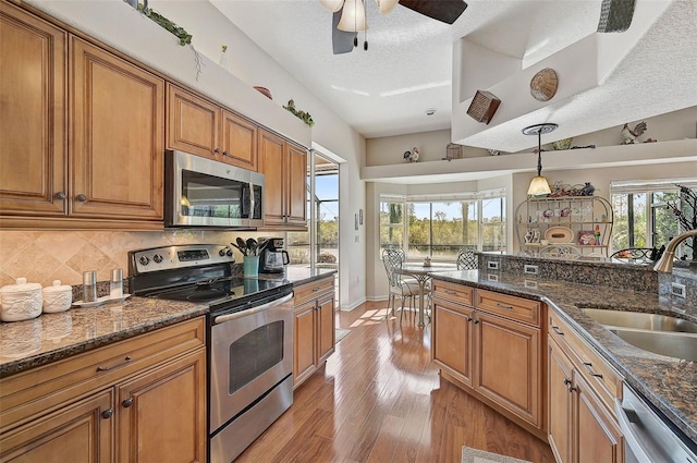 kitchen with sink, a textured ceiling, decorative light fixtures, light hardwood / wood-style floors, and stainless steel appliances