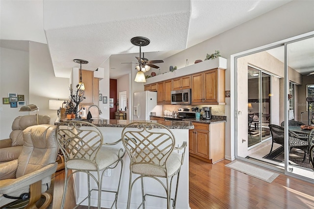 kitchen featuring light hardwood / wood-style flooring, dark stone countertops, a textured ceiling, kitchen peninsula, and stainless steel appliances