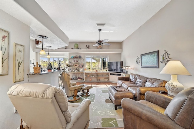 living room with ceiling fan, light wood-type flooring, and a textured ceiling