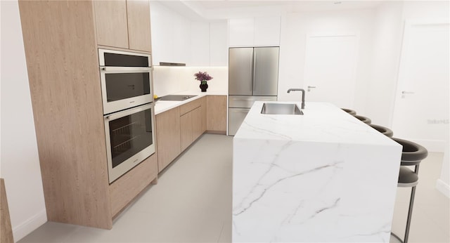 kitchen with white cabinetry, sink, stainless steel appliances, light stone counters, and a center island with sink