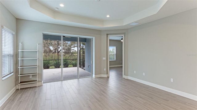 unfurnished room featuring a raised ceiling, light hardwood / wood-style flooring, and ceiling fan