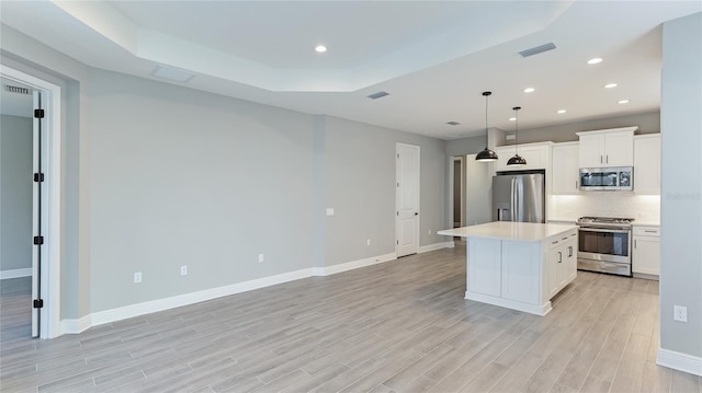 kitchen with stainless steel appliances, white cabinets, light hardwood / wood-style floors, a kitchen island, and hanging light fixtures